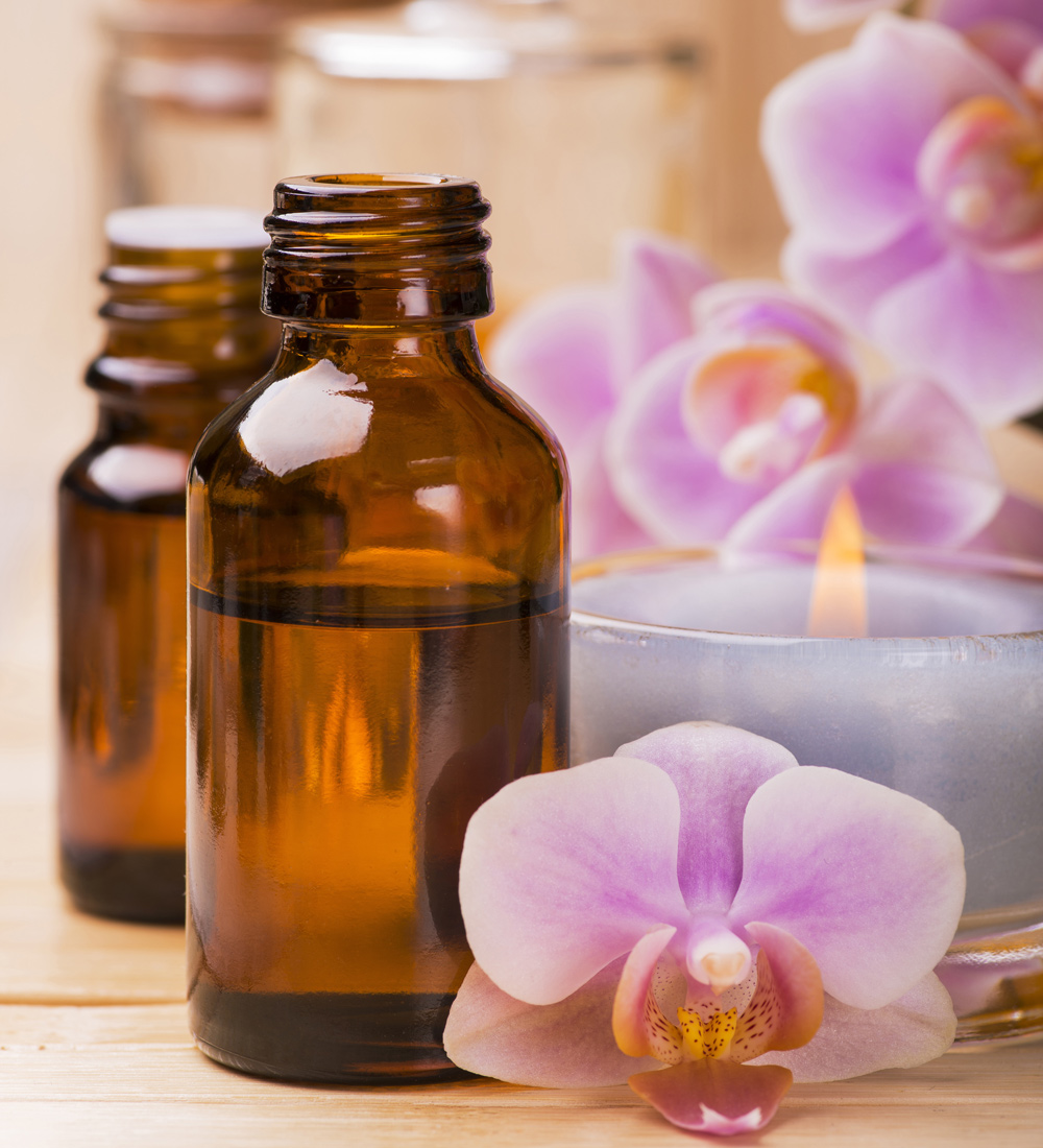 Essential Oil bottles next to a candle and pink orchids.